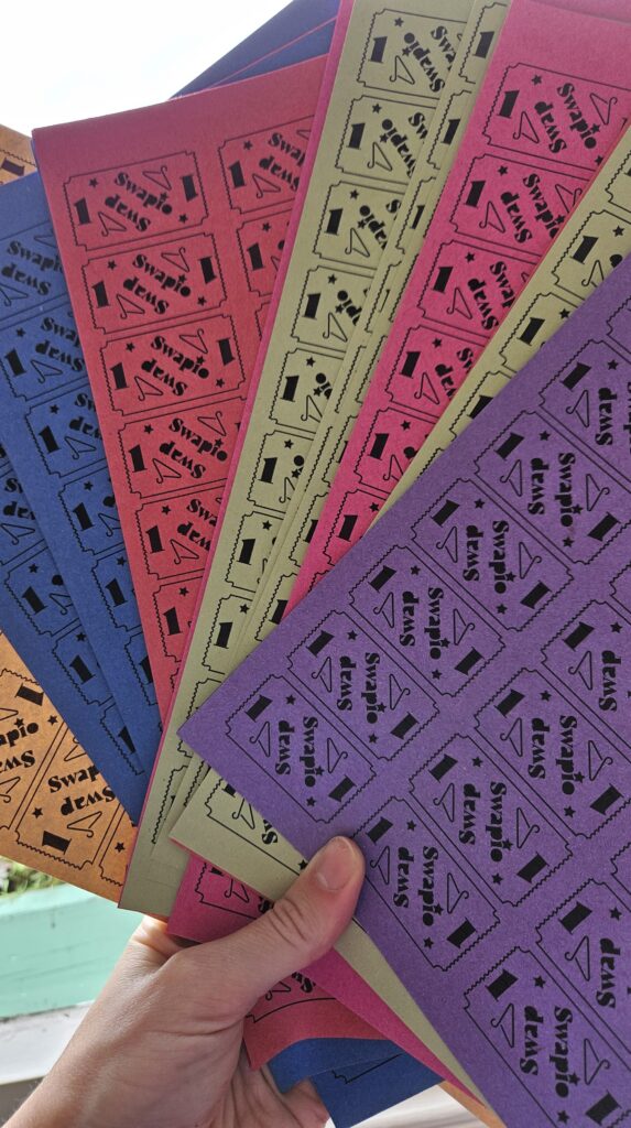 A hand fanning out sheets of Swap Don’t Shop tokens in blue, pink, yellow, orange and purple